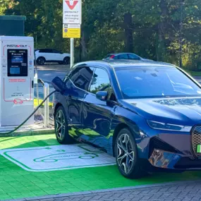 A BMW EV is plugged into an InstaVolt ultra rapid charger in a dedicated green EV bay.