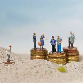 SW Kommunikation Symbolisches Bild von kleinen Figuren auf Geldstapeln im Sand, Darstellung von Gesellschaft und Finanzen