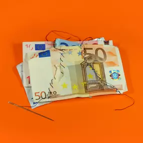 SW Kommunikation Kreatives Foto von zusammengenähten Euro-Scheinen auf orangem Hintergrund, symbolisiert Finanzen und Reparatur