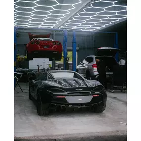 Inside VersionEX Auto’s workshop in Eugene, OR, a black McLaren and red Corvette receive professional service alongside a BMW SUV. The photo highlights the shop’s advanced facility, state-of-the-art lighting, and expertise in both luxury and performance vehicle maintenance.