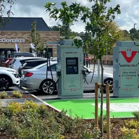 EV charging bays with InstaVolt chargers positioned in front of McDonald's, surrounded by greenery and parked vehicles on Station Road, Buxton.