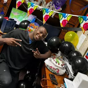 Dr. Olaniran poses at his desk that is decorated with balloons and streamers for his birthday