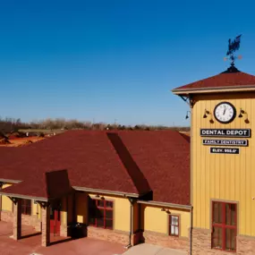 Exterior view of Dental Depot's dentist office on Mustang Rd. with a red roof, yellow exterior, and model train.