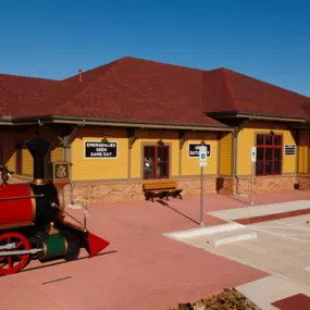 Exterior view of Dental Depot's dentist office on Mustang Rd. with a red roof, yellow exterior, and model train.