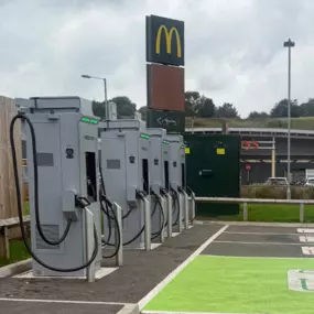 This image shows a row of InstaVolt ultra-rapid electric vehicle chargers at the Leek A523 McDonald’s site. Marked EV bays are clearly visible, with McDonald’s signage above and retail units like Sainsbury’s in the background.