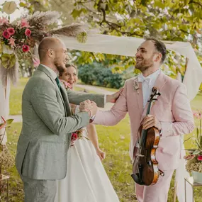 dunkelgoldmusik | Hochzeits- und Veranstaltungsmusik Fröhliche Szene: Violinist gratuliert Brautpaar bei Trauung im Freien mit romantischer Musik. Foto von Lisa Reich.