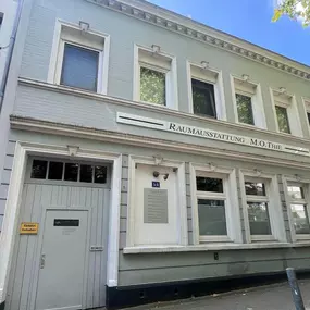 Martin Otto Thie Raumgestaltung Inh. Aline Sander e.K. Außenansicht eines traditionellen Werkstattgebäudes mit Schriftzug und klarer Struktur. Verbindung von Handwerkstradition und moderner Innenraumgestaltung.