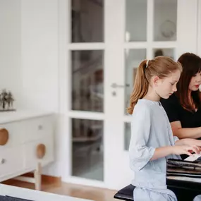 Elite Musik Ein junges Mädchen übt konzentriert am Klavier, während eine Lehrkraft sie professionell begleitet.