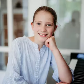 Elite Musik Ein fröhliches Mädchen am Klavier, ideal für Inhalte rund um Musikunterricht und kreative Förderung.