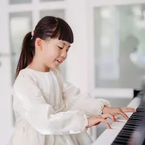 Elite Musik Ein elegantes Motiv eines Kindes im weißen Kleid beim Klavierspielen – ideal für kreative oder pädagogische Themen.