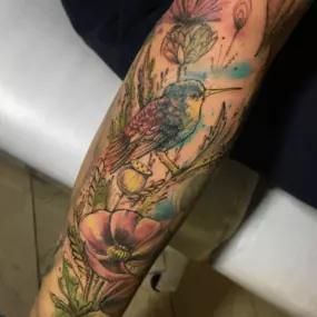 Schmierfink & Robird lebendiges tattoo eines kolibris mit floralen elementen, farbenprächtiger aquarellstil kombiniert mit feiner linienarbeit für natürliche dynamik