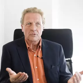Ein Mann spricht in einem professionellen Umfeld vor der Kamera. Seine Gestik und Mimik vermitteln Offenheit, Kompetenz und Vertrauen.