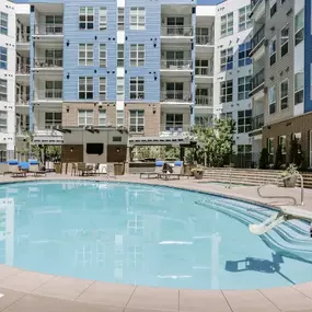 Modern mid-rise apartment building with resort-style amenities including a swimming pool, fitness center, and spacious balconies in an urban neighborhood.