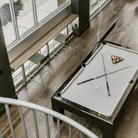 This image features a stylish resident game lounge with a sleek pool table, wood-style flooring, and floor-to-ceiling windows that brighten the space. Comfortable seating and a modern design create an inviting area for residents to relax and socialize.