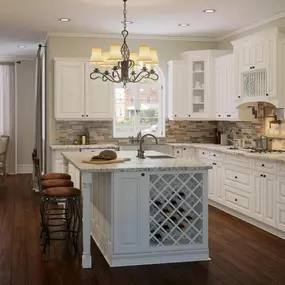 A traditional kitchen featuring white paneled cabinets, dark wood floors, a center island with a built-in wine rack, and a casual dining area.
