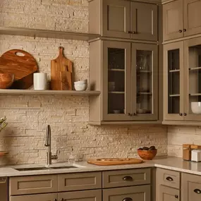 A cozy kitchen featuring taupe-colored shaker cabinets, a rough stacked stone tile backsplash, a floating shelf, and glass-front upper cabinets.