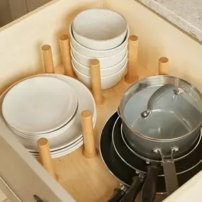 An open kitchen drawer features a custom wooden pegboard system organizing stacks of white plates, bowls, and nested pots and pans.