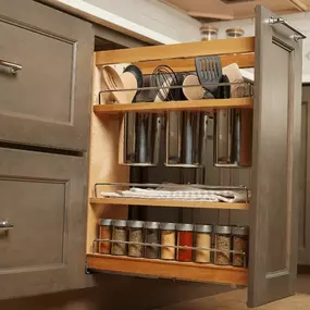 A slide-out base cabinet organizer reveals wooden shelves holding cooking utensils, spice jars, and a pull-out towel rack for maximized storage.