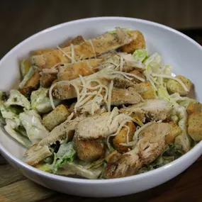 A freshly grilled chicken breast atop chopped romaine lettuce, tossed with parmesan cheese, croutons, and caesar dressing