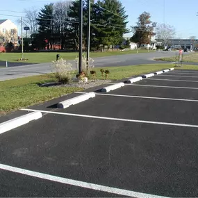 Freshly paved asphalt parking lot with bright white striping and installed concrete wheel stops. Construction Material Asphalt & Sealcoating LLC accessories and paving in Ocala, FL.