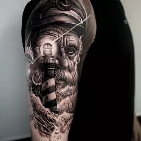 Black and Grey Realistic Tattoo auf dem Oberarm. Ein Leuchtturm und ein alter Seeman.