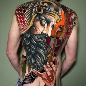 Ares oder Mars als Backpiece im Neotraditional Style, ein Gesicht mit Helm und Bart und eine Hand und ein Schwert. kräftiges rot und schwarz ist zu sehen und andere farbliche Akzente