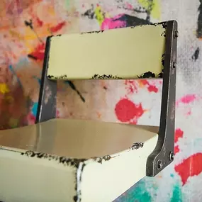 Innenraum: Nahaufnahme eines Vintage-Metallstuhls vor bunt gesprenkeltem Studiohintergrund.