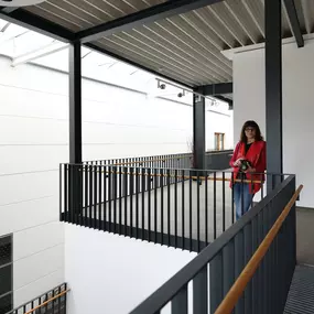 Person in roter Jacke mit Kamera steht im modernen Atrium mit Stahlträgern, Oberlicht und Geländern.