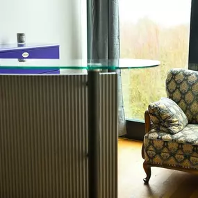 Empfang im Fotostudio: Tresen mit Glasplatte und geriffelter Front, gemütlicher Wartebereich mit Vintage-Sofa, Sideboard mit Bilderrahmen, bodentiefe Fenster mit Blick ins Grüne. Bereich für Begrüßung und Beratung bei ‚ANNETTE STIER – Fotografie‘.