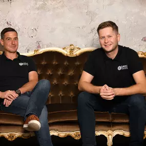 Businessportrait zweier Geschäftsführer auf Vintage-Sofa im Studio-Set mit strukturierter Wand. Ruhige, professionelle Bildsprache für Website, PR, LinkedIn und Recruiting – fotografiert von ‚ANNETTE STIER – Fotografie‘.