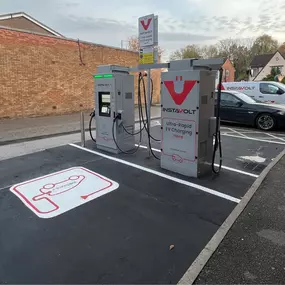 Dual InstaVolt ultra-rapid chargers installed on freshly painted EV bays, with a branded van parked nearby and residential houses in view beyond the car park.