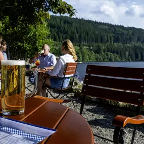 Der Biergarten des Maritim Hotels Titisee lädt mit gemütlichen Sitzplätzen im Freien und rustikalem Charme zum Entspannen ein. Gäste genießen erfrischende Getränke und Snacks in einer angenehmen Umgebung.