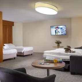 Das Familienzimmer im Maritim Hotel Stuttgart bietet Komfort für die ganze Familie, mit Doppelbett, Schlafsofa, Arbeitsbereich und Blick auf den Hoppenlau-Park.