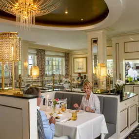 Im Orangerie-Restaurant schaffen zahlreiche Fenster und elegante Kronleuchter eine edle, lichtdurchflutete Atmosphäre. Die gedeckten Tische sind mit feinem Geschirr und stilvollen Deko-Elementen versehen.