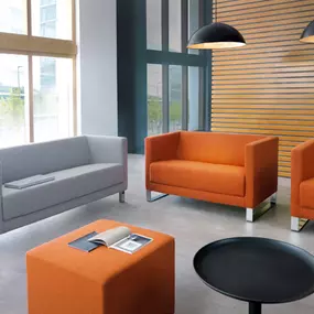 Eine stilvolle Lounge-Ecke mit modernen Sitzmöbeln und durchdachtem Design. Die Kombination aus kräftigen Farben, hochwertiger Verarbeitung und einer offenen Raumgestaltung schafft eine einladende Atmosphäre für produktive Meetings und entspannte Pausen.