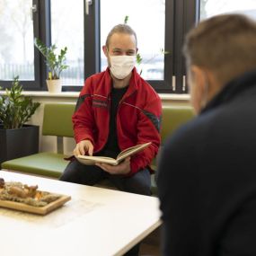 Johanniter-Fachbereichsleiter Marcel Schmidt liest einem Mann vor. Er möchte mit diesem Beispiel viele Männer für die ehrenamtliche Hospizarbeit gewinnen.