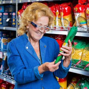 Eine Dame liest im Supermarkt die Details mithilfe einer Licht-Lupenbrille von VIDEBIS