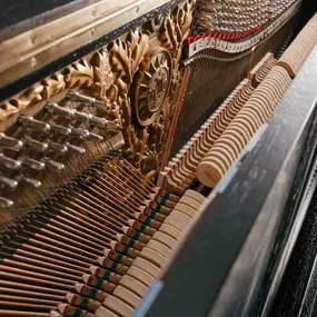 Detailaufnahme der Klaviermechanik mit Saiten, Hämmern und kunstvoller Verzierung. Veranschaulicht die präzise Handwerkskunst im Klavierbau.