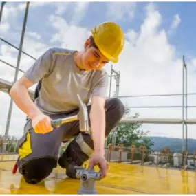 Montage-Elektiker Lehrling der mit Hammer und Helm ausgerüstet auf der Baustelle bei der Arbeit ist.