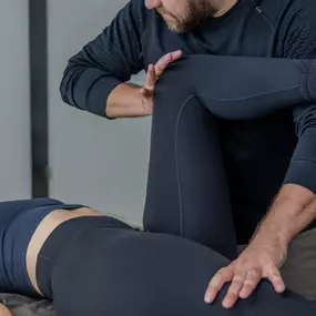 Das Bild zeigt eine physiotherapeutische Anwendung mit kinesiologischen Elementen, bei der der Therapeut gezielt mit den Beinen des Patienten arbeitet.