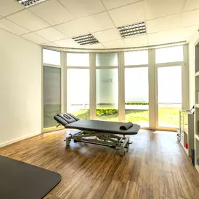 Der großzügige, lichtdurchflutete Behandlungsraum mit moderner Therapieliege schafft eine angenehme Umgebung für individuelle physiotherapeutische Anwendungen.