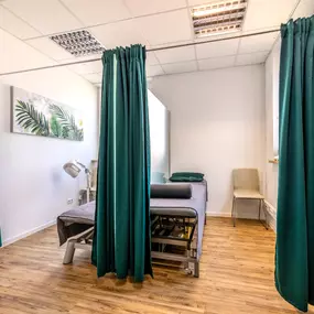 Das Bild zeigt zwei geöffnete Behandlungskabinen mit Vorhängen und Einblick auf die Therapieliegen.