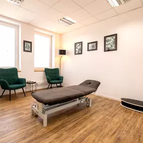 Das Bild zeigt einen ruhigen Behandlungsraum mit einer Therapieliege und zwei Stühlen – funktional und klar eingerichtet.