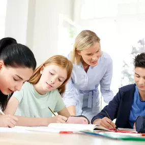 Nachhilfelehrerin unterstützt ihre Schüler beim Lernen am Tisch.