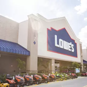 Exterior photo of entrance to Lowe's Home Improvement with plants and lawn mowers outside.