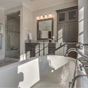 A view from the tub into a design featuring painted grey bathroom vanity cabinets.