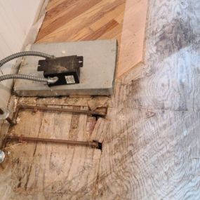 Pictured here is Minneapolis water damage restoration in a main-level laundry room.  If you look at the area of subflooring near the water pipe, you can see black mold.