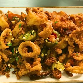 A platter of golden fried calamari at Slacks Oyster House, Plainridge Park Casino, garnished with grilled lemon and served with a side of marinara sauce. The calamari is crispy and tender, a popular appetizer choice at this seafood-focused restaurant.