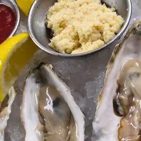 A plate of fresh oysters on the half shell served on ice at Slacks Oyster House, accompanied by lemon wedges, cocktail sauce, and horseradish. The oysters are presented in a classic style, ready to be enjoyed with a squeeze of lemon or a dash of sauce.