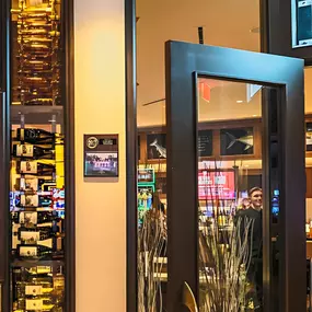 The entrance to Slacks Oyster House at Plainridge Park Casino, with a welcoming atmosphere that features warm lighting and a modern design. The restaurant's logo is prominently displayed, surrounded by a showcase of wine bottles, inviting guests to enjoy a luxurious dining experience.